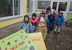 Dzieci stoją przed biblioteką z książkami, które wypożyczyły o prawach dziecka.