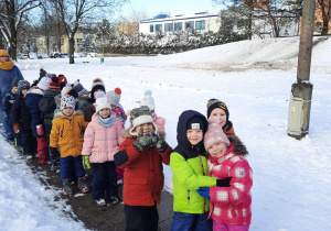 Dzieci stojąc w parach pozują do zdjęcia w zimowej scenerii