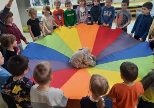 Grupa dzieci stoi wokół chusty animacyjnej, bawią się.