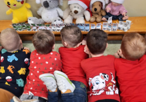 Chłopcy w mikołajkowych strojach leżą na dywanie, patrząc na małe podarunki.