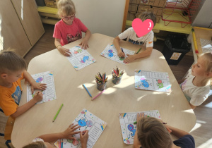 Dzieci siedzą przy stoliku i kolorują wg instrukcji słownej nauczyciela