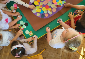 Grupa dzieci wypełnia dużą kropkę za pomocą kół origami w rożnym kolorze i rozmiarze