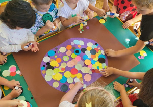 Grupa dzieci wypełnia dużą kropkę za pomocą kół origami w rożnym kolorze i rozmiarze