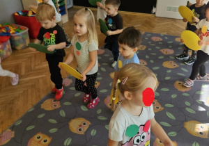 Dzieci biegna po dywanie, trzymając kolorowe krążki.