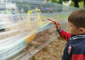 chłopiec maluje farbami po folii rozciągnięej pomiędzy drzewami