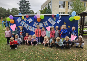Dzieci stoją w szeregu na tle dekoracji z napisem Dzień Przedszkolaka