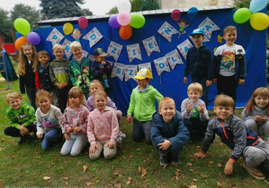 Dzieci stoją w szeregu na tle dekoracji z napisem Dzień Przedszkolaka