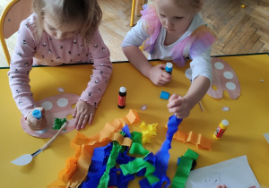 Dziewczynki formują z bibuły kulki i przyklejają na paletę