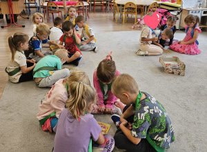 Dzieci siedzą na dywanie, pracują w małych zespołach.