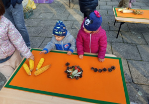 Dzieci z rodzicami układają jesienne obrazy z kukurydzy, szyszek, ksztanów