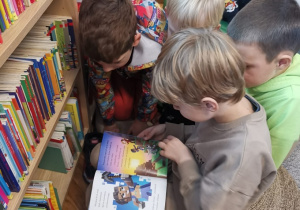 Chłopcy oglądają wybraną przez siebie książkę w bibliotece