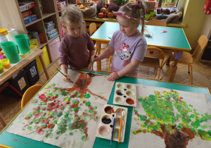 Dwie dziewczynki malują brązową farbą pień drzewa