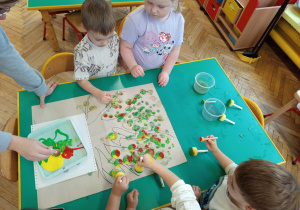 Dzieci stemplują farbami owoce na gałęziach drzewa