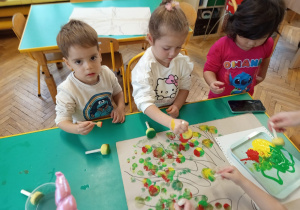 Dzieci stemplują farbami owoce na gałęziach drzewa