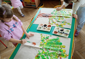 Dwie dziewczynki malują brązową farbą pień drzewa