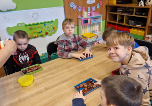 Dzieci wykonują sowę w słoiku wykorzystując kasztany i kolorowe piórka