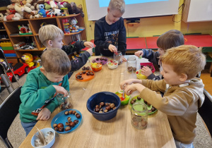 Dzieci wykonują sowę w słoiku wykorzystując kasztany i kolorowe piórka