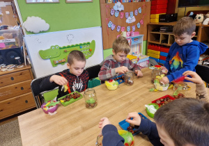 Dzieci wykonują sowę w słoiku wykorzystując kasztany i kolorowe piórka