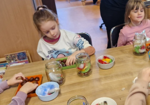 Dzieci wykonują sowę w słoiku wykorzystując kasztany i kolorowe piórka