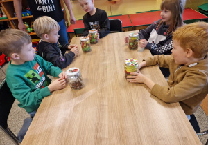 Dzieci wykonują sowę w słoiku wykorzystując kasztany i kolorowe piórka