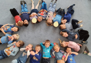 Dzieci w niebieskich strojach leżą w kole na dywanie