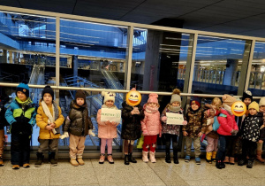 Dzieci stoją na dworcu z plakatem logo firmy Elester