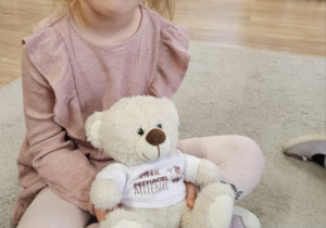 Dziewczynka siedzi na dywanie z misiem