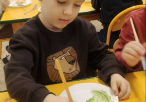 Chłopiec w opasce z uszami maluje talerzyk