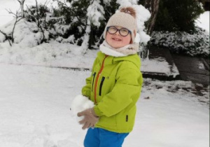 Chłopiec stoi z dużą kulką śniegową