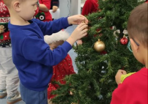 Chłopczyk stoi przy choince i zakłada bombkę