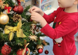 Chłopiec w czerwonej koszulce wiesza bombkę na choince