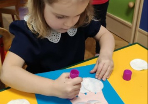 Dziewczynka wykleja brodę Mikołaja na pracy plastycznej z rączki