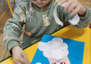 Chłopczyk siedzi przy stoliku i wykleja śnieżynki na swojej pracy