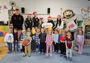 Dzieci z grupy Skrzaty na wspólnym zdjęciu z koszykarzami, maskotką klubu i choinką
