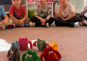Dzieci siedzą na dywanie, patrzą na maskotki przedstawiające emocje.