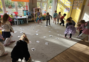 Dzieci na dywanie bawią się kartonikami z literami