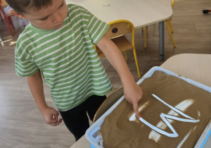 Chłopiec kreśli literę w piasku