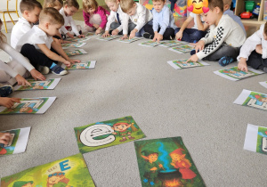 Dzieci siedząc na dywanie kreślą litery na planszach