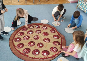 Dzieci układają składniki na dużej macie pizzy