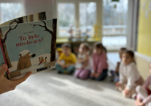 Psycholog czyta ksiażkę, a dzieci siedzą na dywanie i słuchają