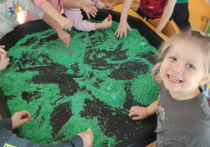 Dzieci stoją przy pojemniku wielorakich aktywności i bawią się kolorowym ryżem