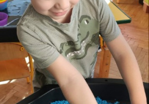 Chłopiec bawi się dinozaurem w kolorowym ryżu