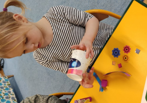 Dziewczynka przykleja elementy do kubeczka robiąc robota